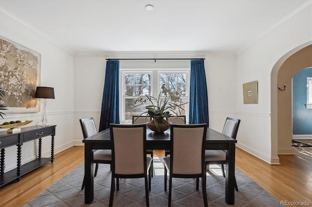 dining space featuring arched walkways, crown molding, wood finished floors, and baseboards