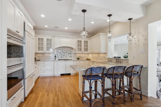 kitchen featuring appliances with stainless steel finishes, a breakfast bar area, a peninsula, premium range hood, and a sink