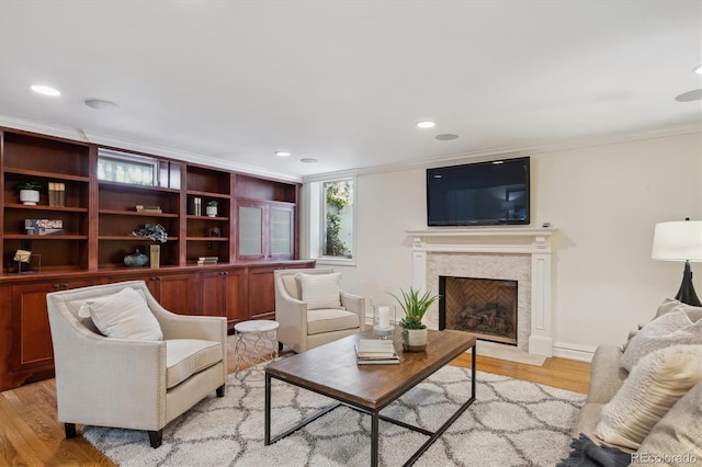 living area featuring recessed lighting, a premium fireplace, baseboards, ornamental molding, and light wood finished floors