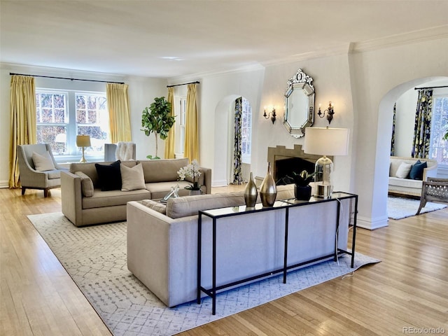 living area with arched walkways, a fireplace, ornamental molding, wood finished floors, and baseboards