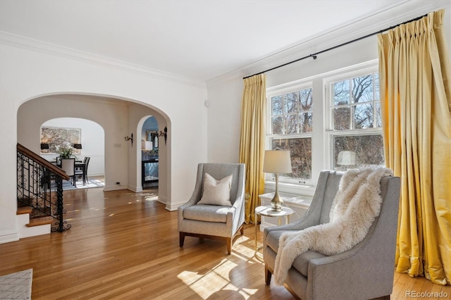 living area with arched walkways, ornamental molding, stairway, and light wood-style flooring