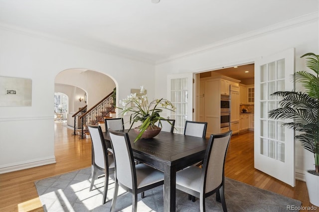 dining room featuring stairs, arched walkways, wood finished floors, and ornamental molding