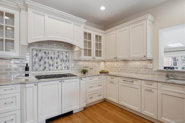 kitchen featuring stainless steel gas cooktop, light wood-style flooring, glass insert cabinets, white cabinets, and a sink