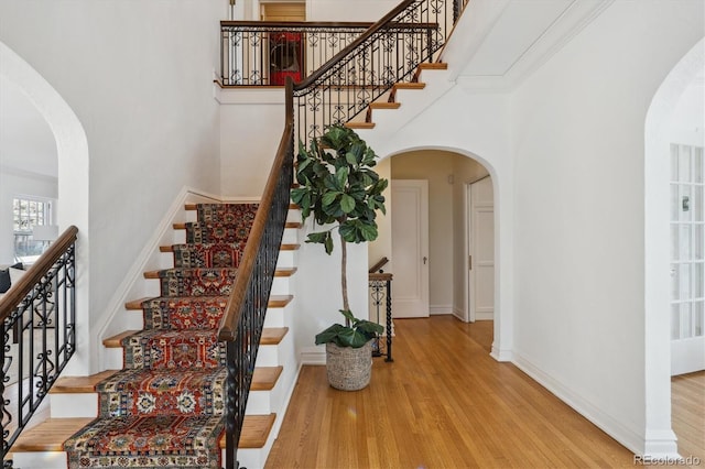 stairs featuring arched walkways, a high ceiling, and wood finished floors