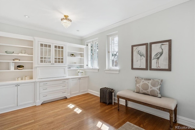 living area with baseboards, radiator heating unit, light wood-type flooring, and crown molding