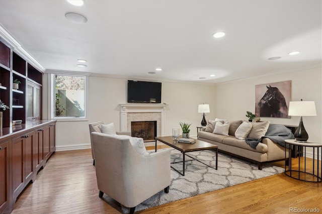 living room featuring ornamental molding, recessed lighting, a fireplace, and light wood-style flooring