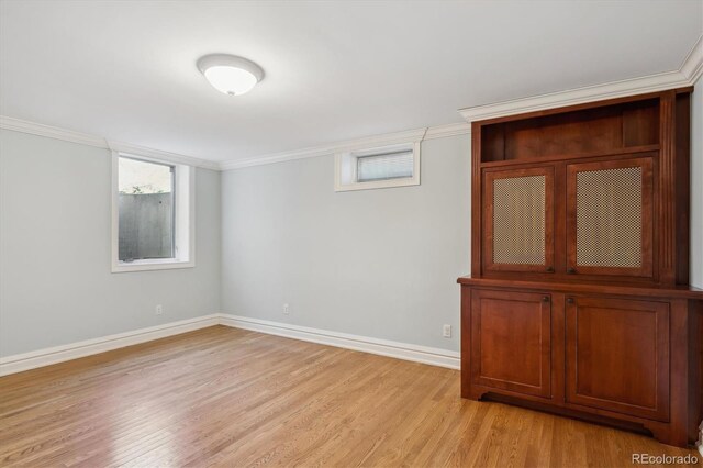 spare room with ornamental molding, light wood-style floors, and baseboards