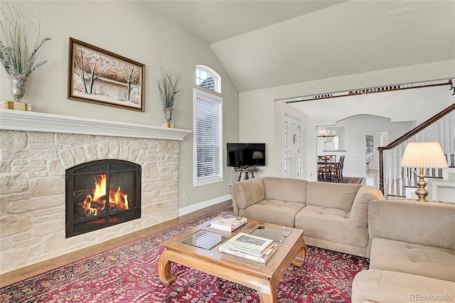 living area with lofted ceiling, a stone fireplace, wood finished floors, and baseboards