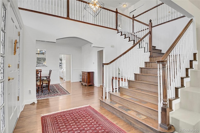 entrance foyer featuring arched walkways, a high ceiling, wood finished floors, baseboards, and stairs