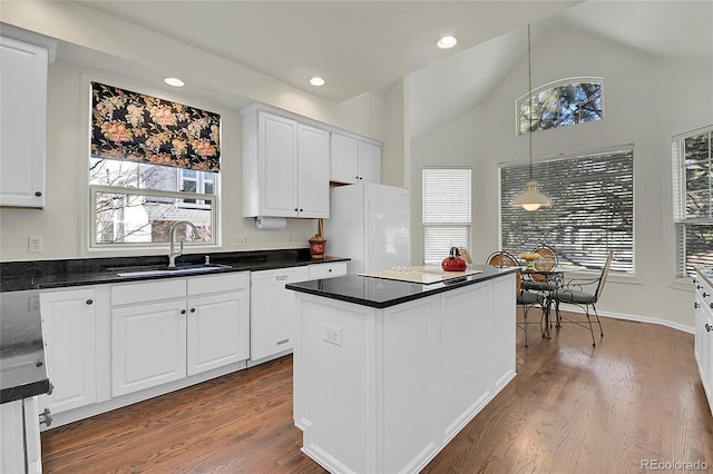 kitchen with white appliances, a sink, white cabinetry, dark countertops, and decorative light fixtures