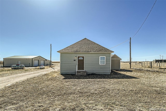 rear view of house with roof with shingles, a detached garage, and an outbuilding