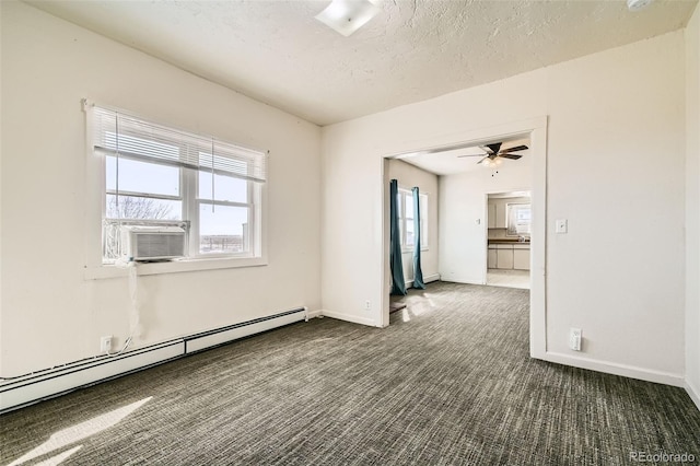 spare room with a textured ceiling, baseboard heating, dark carpet, and a healthy amount of sunlight