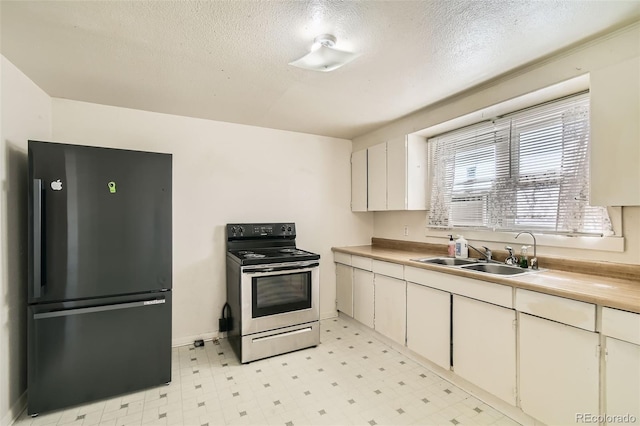 kitchen with stainless steel range with electric stovetop, freestanding refrigerator, a sink, and light floors