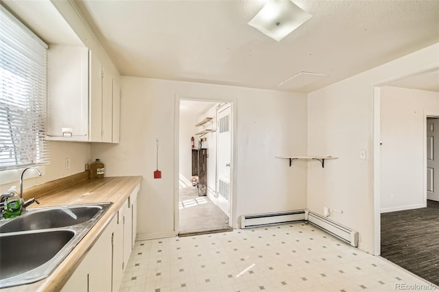 kitchen with a sink, white cabinetry, light countertops, baseboard heating, and light floors