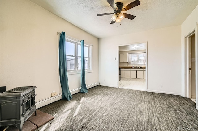 unfurnished living room featuring a baseboard radiator, ceiling fan, a wood stove, a textured ceiling, and carpet flooring