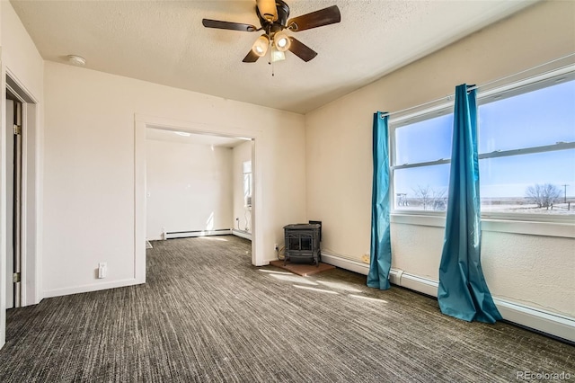 spare room with carpet floors, a wood stove, a baseboard heating unit, and a textured ceiling