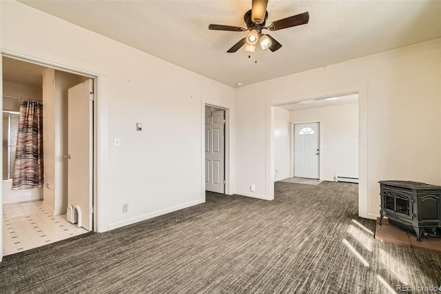 unfurnished living room featuring a baseboard heating unit, a wood stove, carpet floors, and a ceiling fan