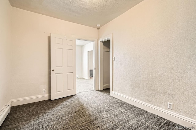 carpeted spare room featuring a textured ceiling, a textured wall, baseboard heating, and baseboards