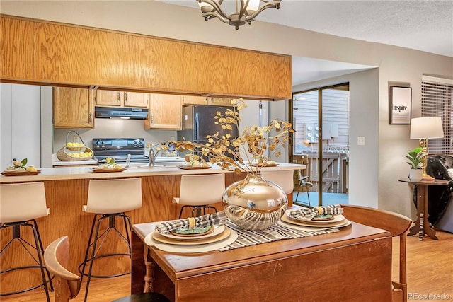 kitchen with a kitchen bar, light wood-type flooring, under cabinet range hood, electric range oven, and freestanding refrigerator