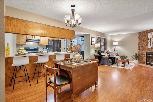dining area featuring a stone fireplace, an inviting chandelier, a textured ceiling, and light wood-style flooring
