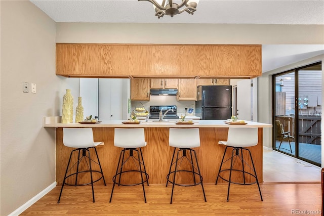 kitchen with light wood-type flooring, a peninsula, light countertops, black appliances, and ventilation hood