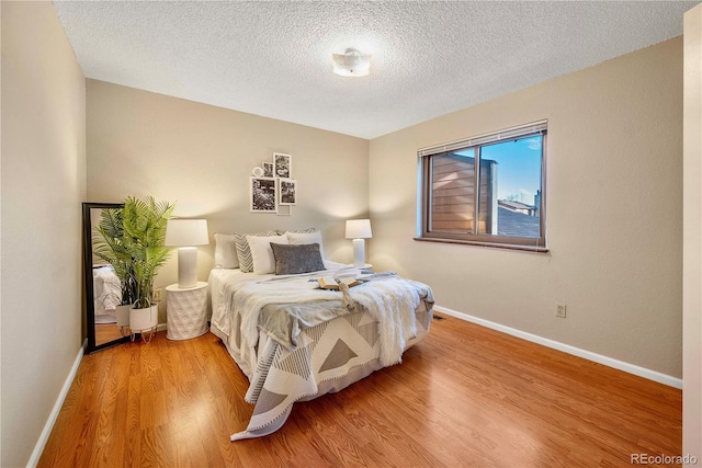 bedroom featuring light wood-style flooring, baseboards, and a textured ceiling