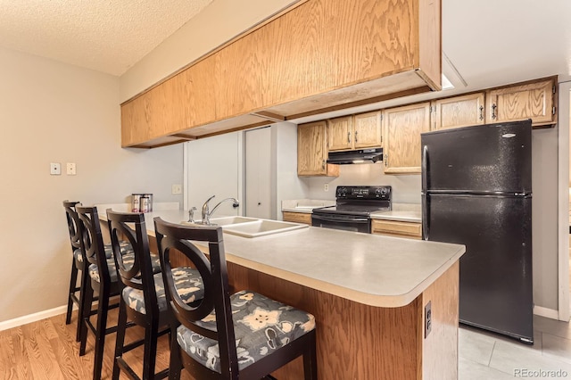 9411 W 89th Cir, Westminster, CO 80021 - kitchen with black appliances, under cabinet range hood, a sink, a peninsula, and light countertops