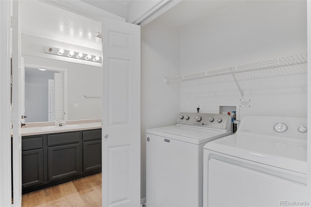 clothes washing area with sink, light hardwood / wood-style flooring, and washing machine and clothes dryer