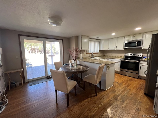 kitchen featuring appliances with stainless steel finishes, kitchen peninsula, dark hardwood / wood-style flooring, and white cabinetry