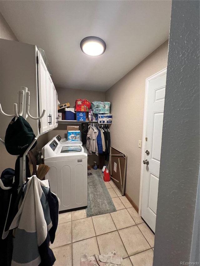 clothes washing area with cabinets, light tile patterned floors, and washing machine and clothes dryer