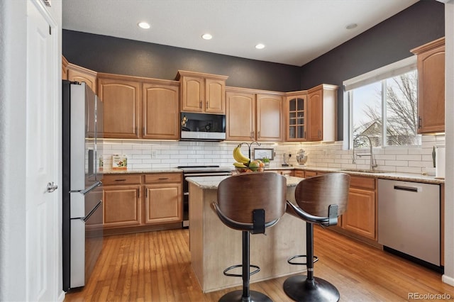 kitchen with sink, light hardwood / wood-style flooring, a kitchen island, stainless steel appliances, and light stone countertops