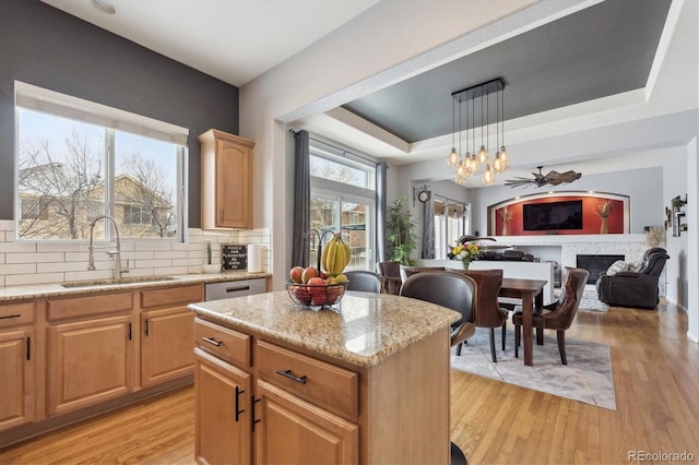 kitchen featuring sink, decorative light fixtures, light wood-type flooring, a tray ceiling, and a kitchen island