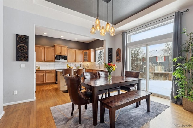 dining area featuring a raised ceiling, sink, and light wood-type flooring