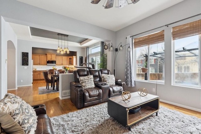 living room featuring a tray ceiling, ceiling fan, and light wood-type flooring