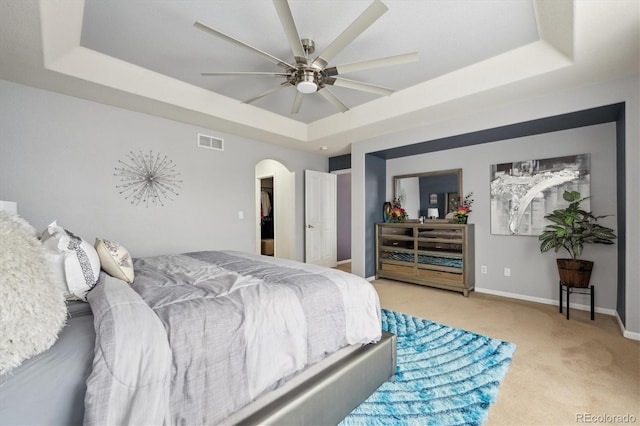 bedroom with ceiling fan, light colored carpet, and a raised ceiling