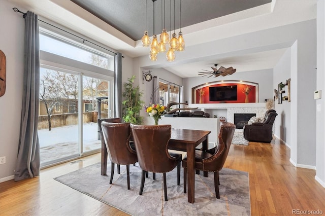 10251 Rifle St, Commerce City, CO 80022 - dining area featuring baseboards, light wood finished floors, a tray ceiling, a glass covered fireplace, and ceiling fan with notable chandelier