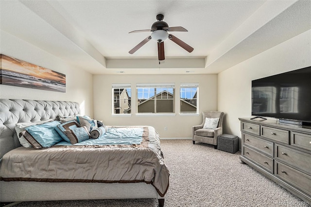 bedroom featuring a raised ceiling, ceiling fan, baseboards, and light colored carpet