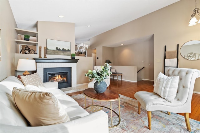 living room with wood-type flooring, built in features, and a brick fireplace