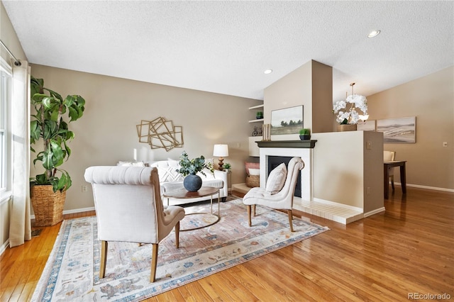 living room with a brick fireplace, a textured ceiling, an inviting chandelier, and light wood-type flooring