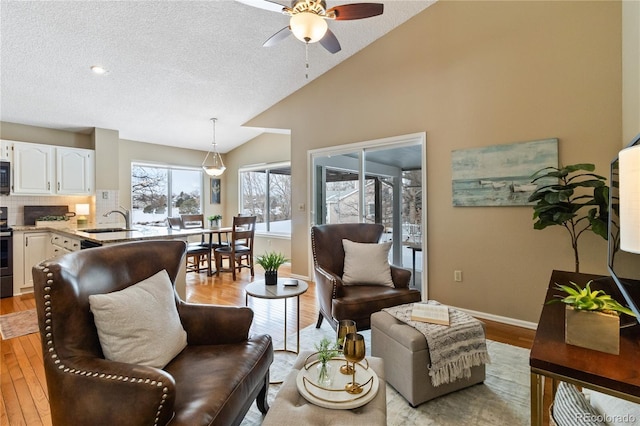 living room featuring vaulted ceiling, ceiling fan, sink, light wood-type flooring, and a textured ceiling