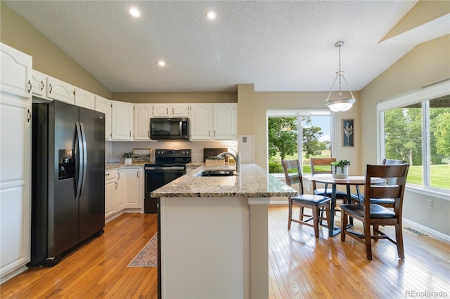 kitchen featuring black appliances, vaulted ceiling, white cabinetry, and sink