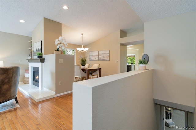 corridor featuring hardwood / wood-style floors, an inviting chandelier, a textured ceiling, and vaulted ceiling