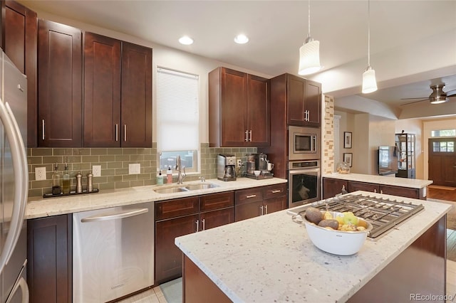 kitchen with stainless steel appliances, hanging light fixtures, a center island, and light stone counters