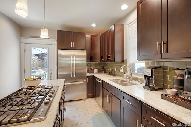 kitchen with pendant lighting, sink, backsplash, light stone counters, and stainless steel appliances