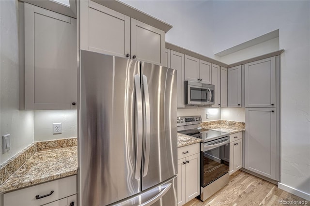 kitchen with light hardwood / wood-style floors, appliances with stainless steel finishes, and light stone counters