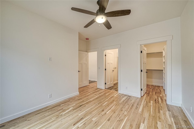 unfurnished bedroom featuring a closet, connected bathroom, light wood-type flooring, a walk in closet, and ceiling fan