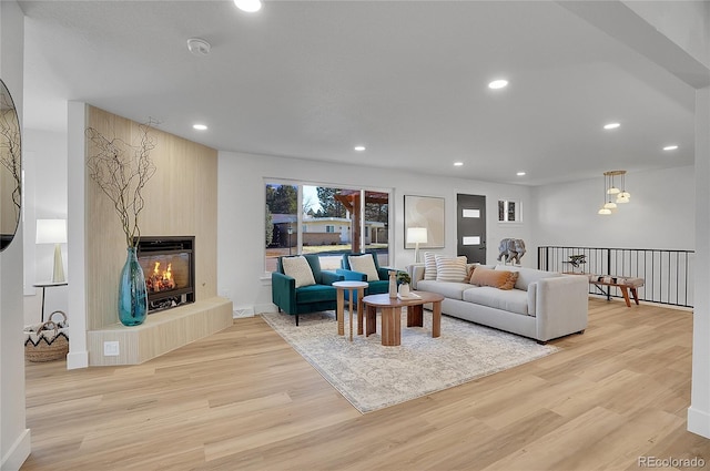 living room featuring a glass covered fireplace, light wood-style flooring, and recessed lighting