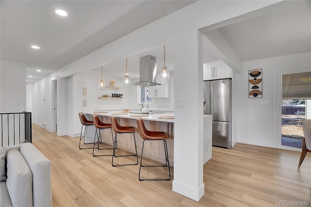 kitchen featuring white cabinetry, light countertops, hanging light fixtures, stainless steel refrigerator with ice dispenser, and island exhaust hood