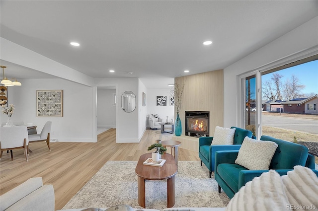 living room featuring light wood-style floors, recessed lighting, a large fireplace, and baseboards