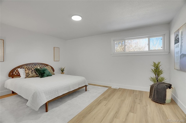 bedroom with a textured ceiling, baseboards, and wood finished floors